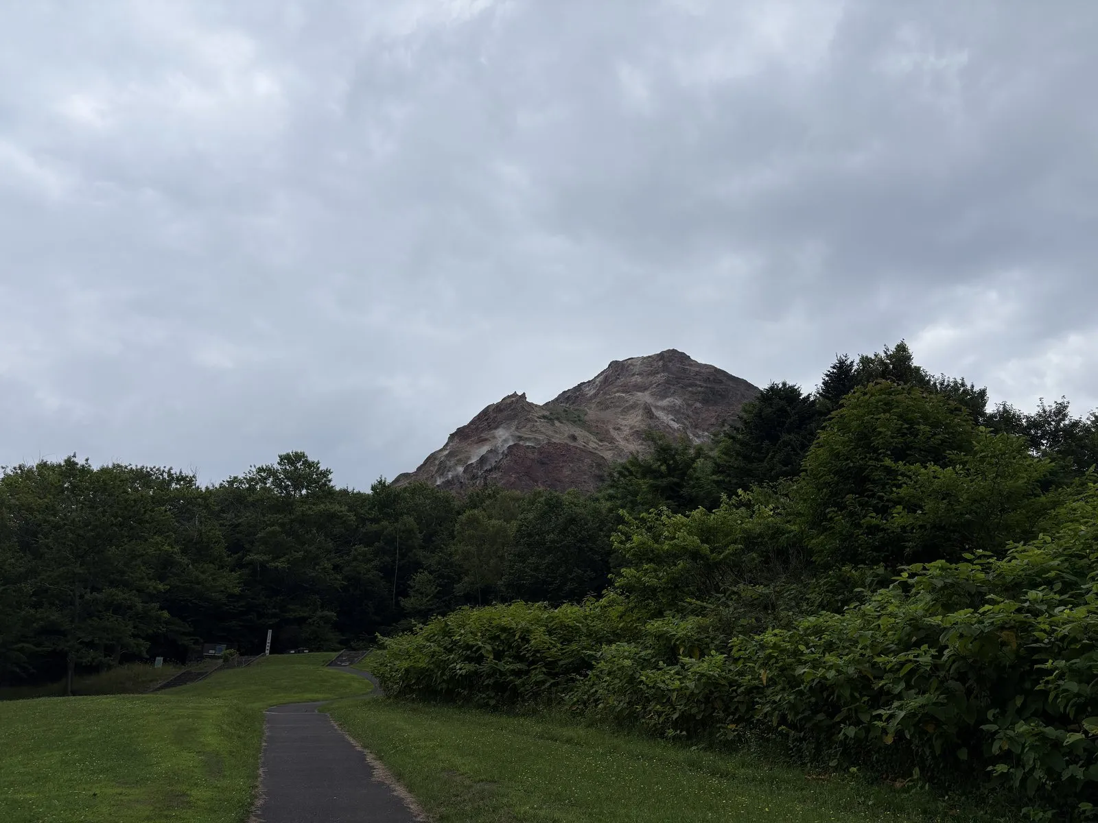 昭和新山。緑の木々の上に、赤茶色の溶岩ドームがむき出しでそびえる